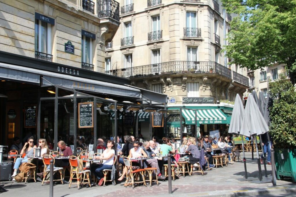 Customers on a crowded, sunny Paris café terrace.