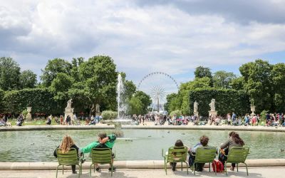 People sitting in green metal chairs around a fountain at the Tuileries Gardens in Paris in summer